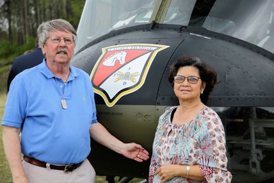 Glenn and his wife pose beside Huey helicopter.